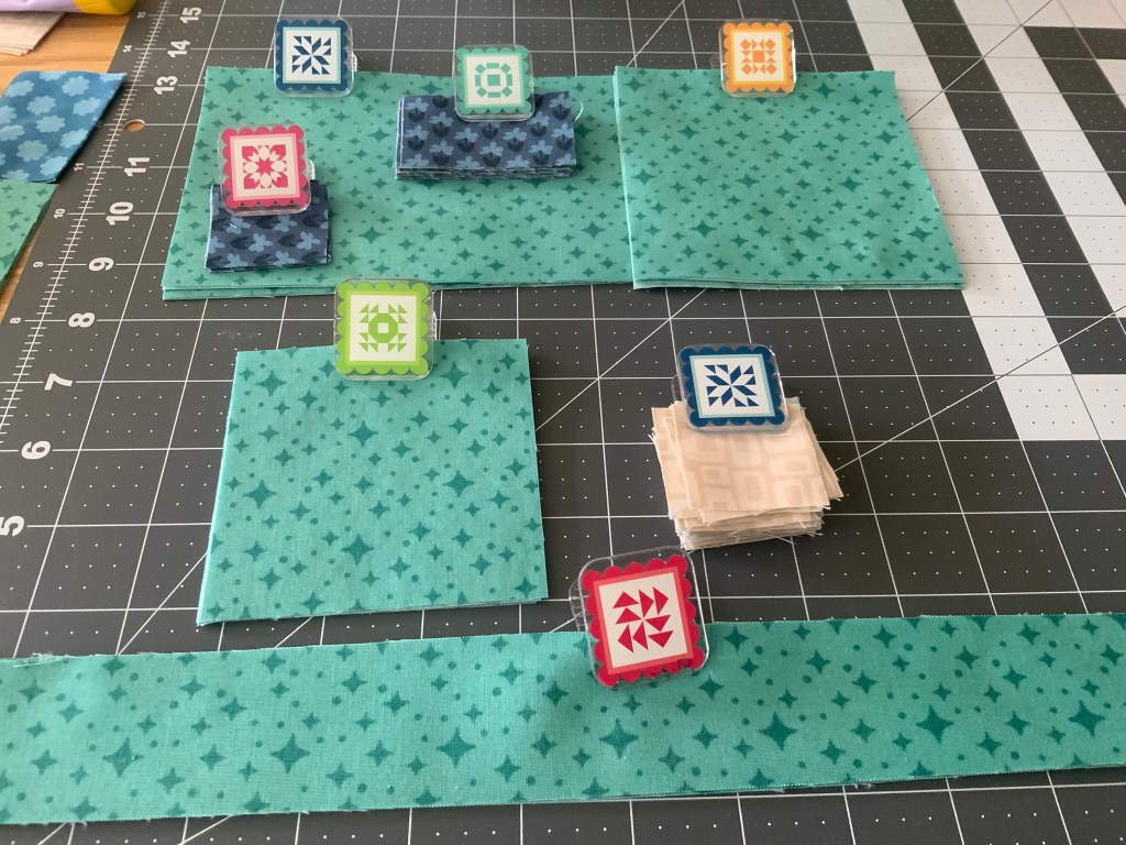 Colorful fabric pieces arranged on a cutting mat with decorative fabric clips on top.