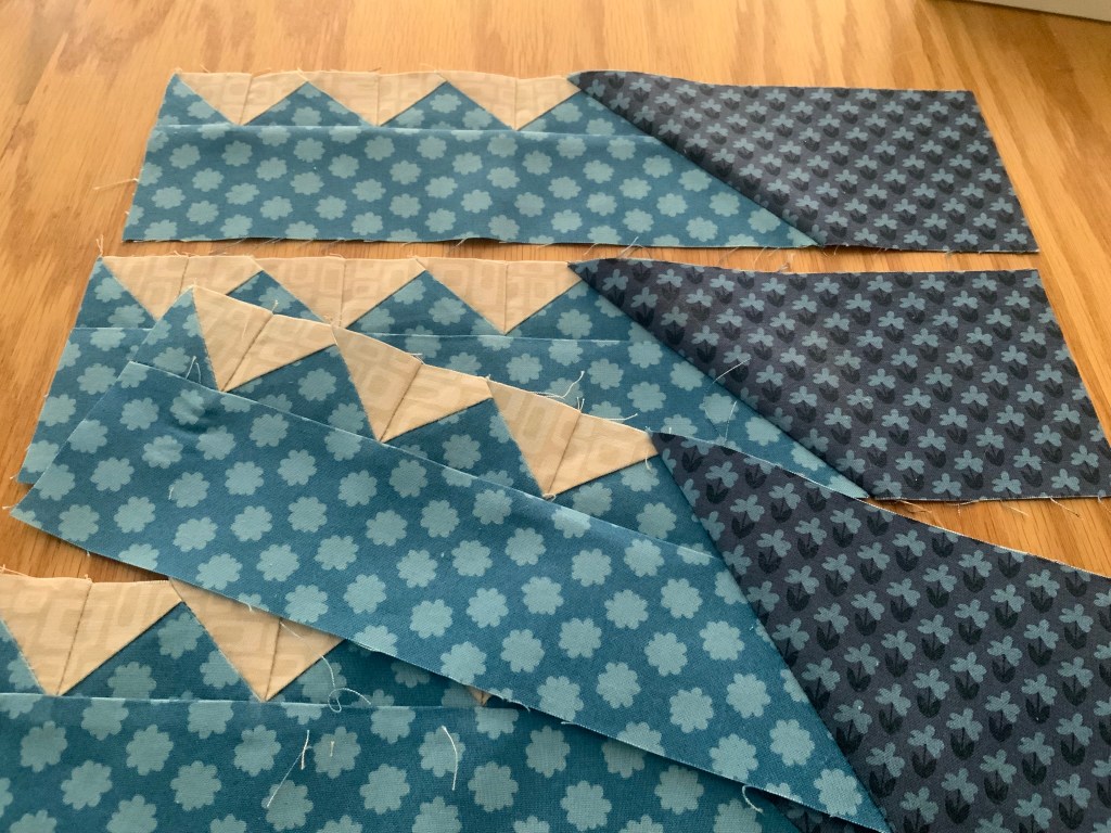 Various fabric cut pieces for quilting, featuring blue floral patterns and cream-colored sections, arranged on a wooden surface.