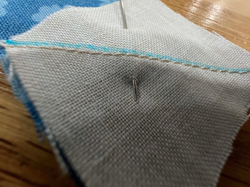 Close-up of fabric pieces being sewn together with a pin and visible stitching.
