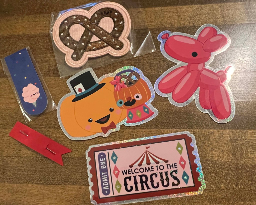 A collection of colorful stickers featuring a pretzel, a pumpkin character with a hat, a pink balloon dog, a cotton candy design, a red ribbon, and a circus ticket that says 'WELCOME TO THE CIRCUS'.